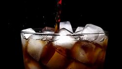 Pouring cola soda into glass of ice with splashes at slow motion on black background Stock Footage