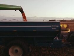 The auger from a combine finishes dumping corn into a wagon and it pulls away with lights on in the early evening. Stock Footage