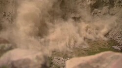 Rocks and dirt fall over a cliff and tumble into water, leaving columns of dust behind. Stock Footage