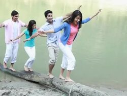Group of friends walking on a fallen tree at riverbank Stock Footage