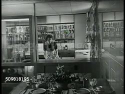 1944: POST-WAR ARCHITECT: INT MS Architects at desk looking over housing plans. CU Artist rendering of house. INT VS Woman in modern kitchen, using modern refrigerator (glass panel) roasting chicken in modern oven. Post-WWII, USA Instructional Video