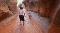 Follow young hiker boy and young hiker girl closely down riverbed through canyon narrows Stock Footage