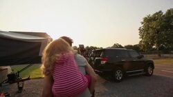 Dad spins happily with small girl on his back with camper in background Stock Footage
