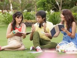 Two teenage girls reading a book with a teenage boy hearing music  Stock Footage