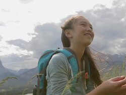 Smiling girl sitting in tall grass below mountains Stock Footage