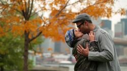 New York couple kiss lovingly in autumn park with Brooklyn Bridge and skyline in background (dolly-shot) Stock Footage