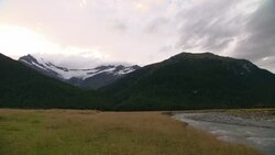 A creek winds across a grassy field at the base of mountains. Stock Footage