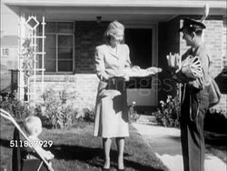 1950: SUBURBS: MAIL DELIVERY: WS Newer homes in suburban neighborhood, woman in suit dress walking to greet mailman. Mailman handing mail to woman, baby in stroller, male joining, woman looking down.  Americana, Boomer, Baby Boom, suburb, Iconic. Instructional Video