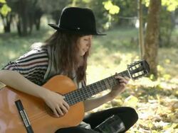 Young woman wearing black hat playing guitar in park, summer. Stock Footage