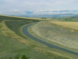 Low altitude aerial over rollings hills and fields in autumn along a two-lane highway near Bozeman, MT Stock Footage
