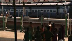 A train passes behind commuters in traditional clothing at a train station in India. Stock Footage
