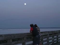 Couple watches super moon rise over the Long Island Sound while standing on pier Stock Footage