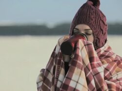 Woman on beach, wrapped in blanket and drinking hot drink Stock Footage