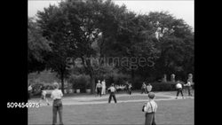 1950: SUPERVISED PLAYGROUND: Boys sitting on park bench cheering. MS Boy umpire trying to figure out which fingers to hold up, two strikes, three balls signal. Baseball game play, boy throwing ball, runner tagged out at home plate. Team sports. Instructional Video