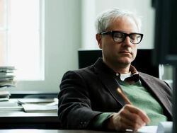 MS smiling businessman seated at workstation in office examining computer monitor and taking notes on notepad Stock Footage