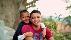 Hispanic teenager and younger brother smile and laugh at camera Stock Footage