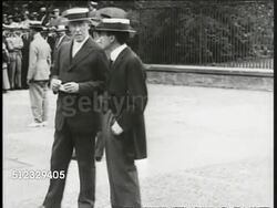 1917: PATRIOTIC: HA XWS People cheering in urban street, American flags & banners on podium below & building BG. President Woodrow Wilson dressed in suit, wide brimmed boater hat, standing outside w/ unidentified man talking, people distant BG. Instructional Video