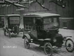 1910s: TRUCKS: WS Ford panel trucks pulling out of line one by one driving on snow covered ground. HA WS Delivery truck in city. LA WS Man unloading milk containers from truck (poor contrast). LA US Mail truck stopping. Man hand cranking dump truck. Instructional Video