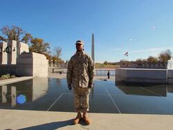 A static shot with a lens flare of a single solider posing for a photo by the WWII Memorial. Stock Footage