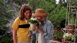 A senior woman smells a pot of flowers and sneezes as her daughter stands next to her and watches surprisingly. Stock Footage