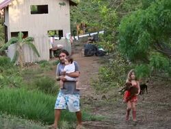 WS Shot of little girl walking while carrying puppy with man walking with carrying baby with cabina, ocean, laundry line, black dog and white dog with palm trees / Montezuma, Punteranes, Costa Rica Stock Footage