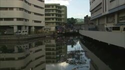 Trash floats in a river near apartment buildings. Stock Footage