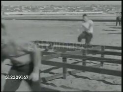1942: U.S. MARINES TRAINING: WS Cadets (AKA 'Rookies, Boots') hurdling, climbing over low exercise fences, wires. WS Cadets climbing over sandbags, pulling themselves up, officer watching BG. VS Men climbing over steep ramps. Training camp Instructional Video