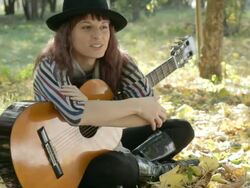 Young woman wearing hat sitting in park outdoors, holding guitar. Stock Footage