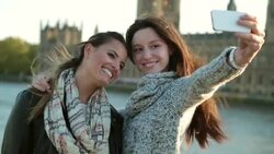 HANDHELD CLOSE UP two young women pose while taking photo with cell phone in London Stock Footage