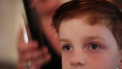 Young boy gets hair combed and trimmed with scissors by mom in family kitchen Stock Footage
