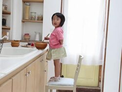 A girl standing on a chair enjoys cooking at the kitchen Stock Footage