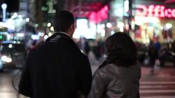 New York couple cross busy street, stopping to kiss amid the bright lights of Times Square as cars drive past Stock Footage