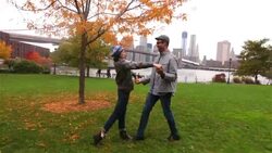 Couple in love embrace in autumn park with Brooklyn Bridge and New York skyline in background Stock Footage