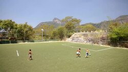 Young Brazilian boys play soccer match on turf field with Christ the Redeemer in distance Stock Footage