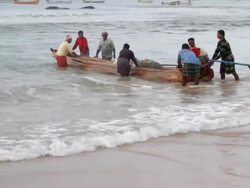 Unidentified Fishermen push a traditional wooden fishing boat into the ocean Stock Footage