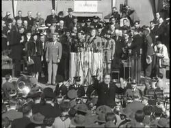 Mayor Fiorello LaGuardia leads the band as Irving Berlin and Kate Smith sing on stage before a large crowd. News Clip