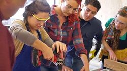 Young woman learns to use power drill in community woodworking shop Stock Footage