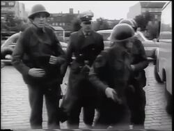 B/W 1961 group of soldiers walking past camera with traffic on Berlin street in background / Cold War Stock Footage