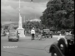 1940: BRITISH WEST INDIES: Black traffic policeman standing in street near monument, cars, bicycles, people on street. WS Residential town gate. Black policeman on horseback directing traffic, British uniform. Instructional Video