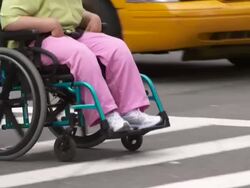 A man pushes a women in a wheel chair across the street Stock Footage