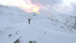 AERIAL Winter mountaineer victoriously raising his hands on mountain top Stock Footage