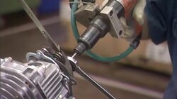 An assembly line worker uses two wrenches and an automated screwdriver as he assembles carburetors. Stock Footage