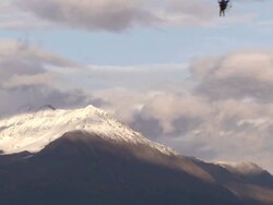 Extreme Long Shot pan-right tilt-up zoom-out - A powerglider soars over a forest near a snow capped mountain / Alaska, USA Stock Footage