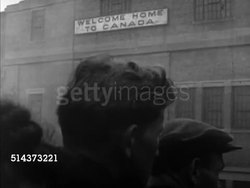 1952: CANADA: IMMIGRATION: TD ANGLED MS Choppy fresh water shoreline w/ thick grasses. WS (Moving with) Passenger ship arriving in harbor, BEHIND People standing on ship deck w/ 'Welcome home to Canada' sign on dock building,  VS Immigrants arriving. Instructional Video