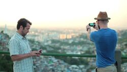 Man checks smartphone while friend snaps photos of the Rio skyline from scenic overlook Stock Footage