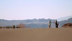 Couple walk down sweltering desert road, young man spots something and runs off to investigate Stock Footage