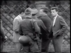 B/W 1961 man smoking cigarettes with others shaking soldier's hand off arm near Berlin Wall Stock Footage