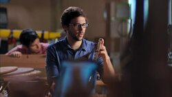 Young craftsman chisels wood in workshop while artist designs frame on laptop computer Stock Footage