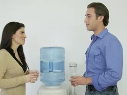 MS woman and young man having discussion standing next to a water cooler Stock Footage