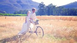 Bride and groom riding bicycle in sunny rural field Stock Footage